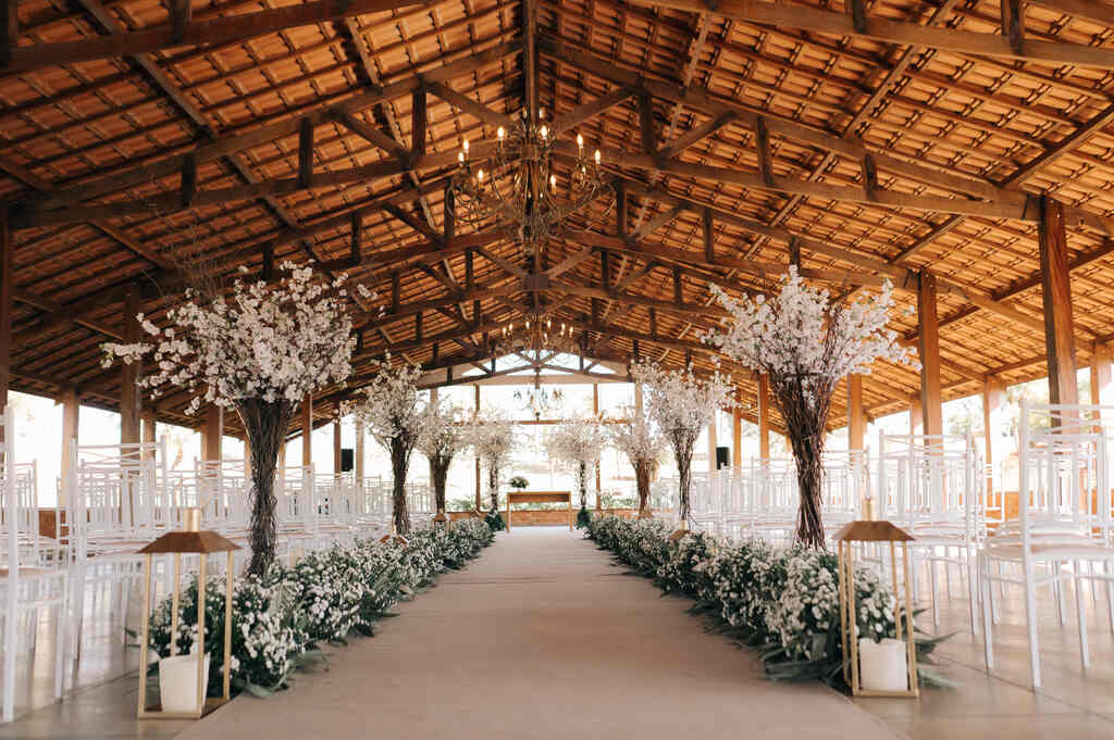 salão rústico de madeira com caminho das noivas com flores brancas e cadeiras tiffany