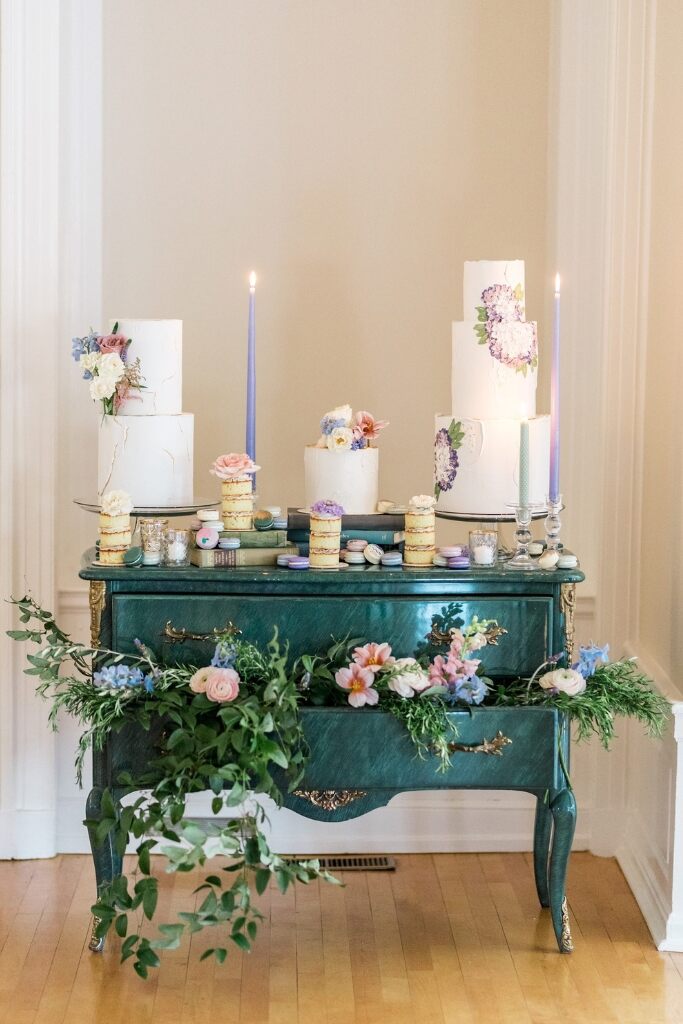 mesa de madeira verde escura com trio de bolos com velas liláses