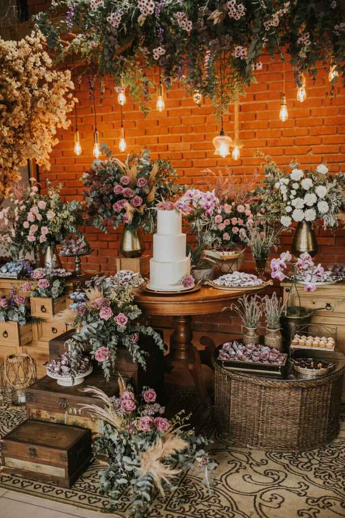 salão rústico com mesas de madeira com doces de casamento e flores brancas e rosas