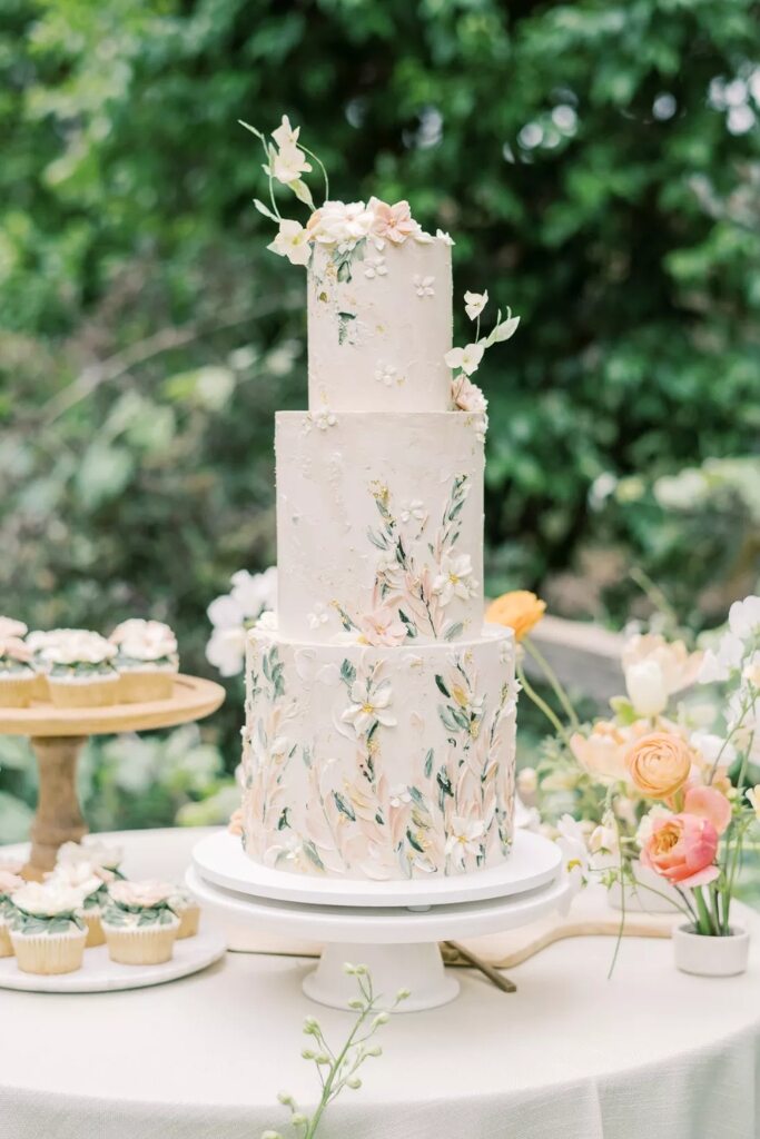 bolo de casamento com estampa de flores e ao lado bandeja com doces