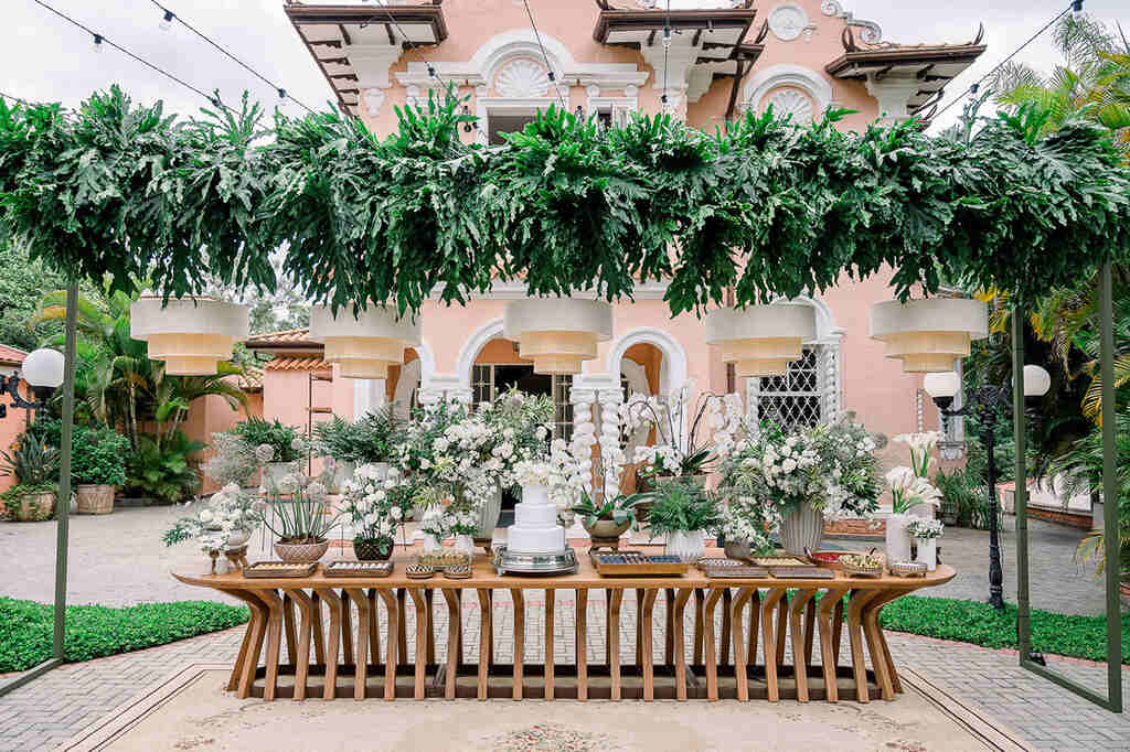 mesa de doces de casamento clássica com plantas pendentes e flores brancas ao ar livre