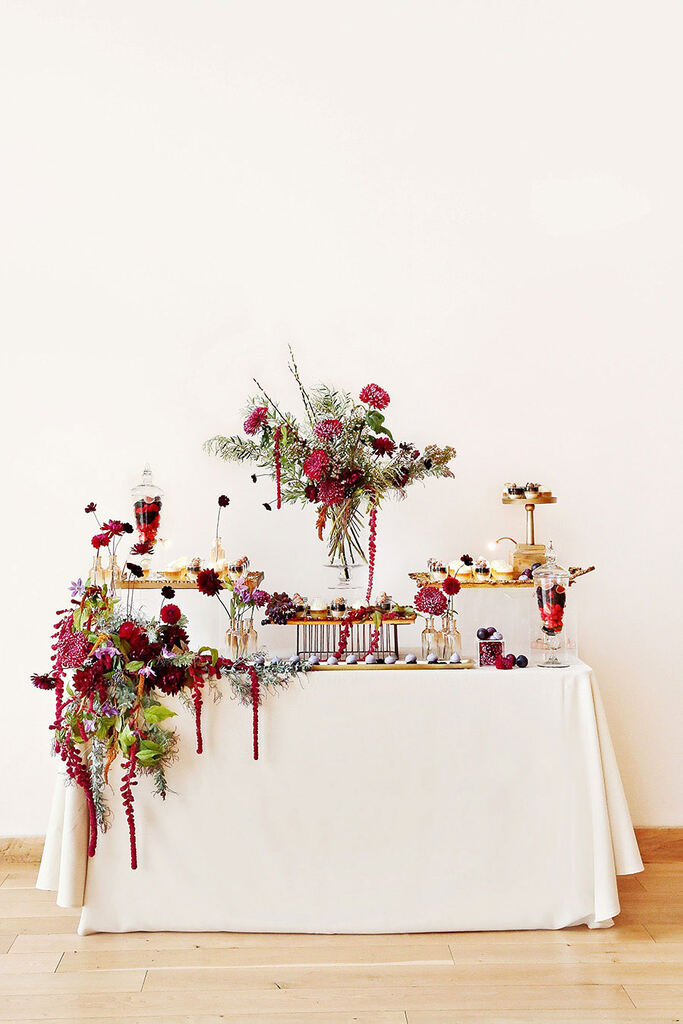 mesa com toalha branca decorada com flores vermelhas e doces de casamento