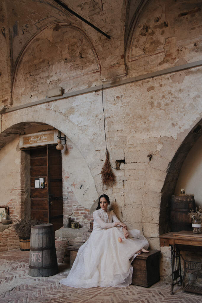 mulher com vestido de noiva vintage com cabelo preso na lateral sentada no salão antigo e rústico na italia