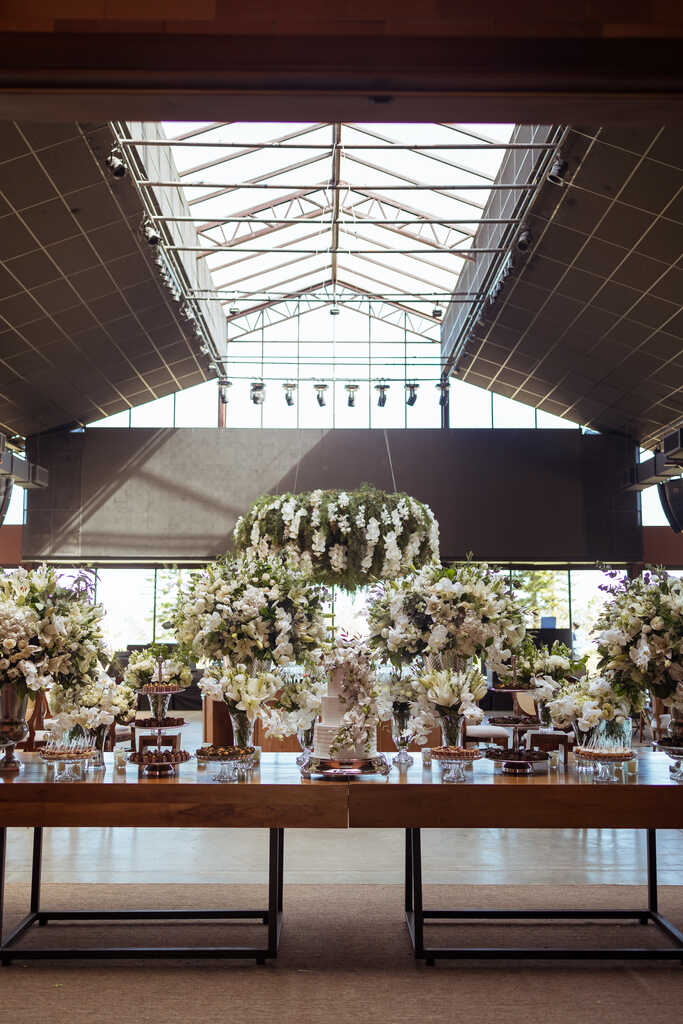 salão moderno com mesa de madeira com bolo de casamento e vasos com flores brancas no estilo clássico contemporâneo
