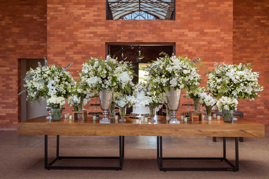salão moderno e rústico com mesa de madeira com bolo de casamento e vasos com flores brancas no estilo clássico contemporâneo