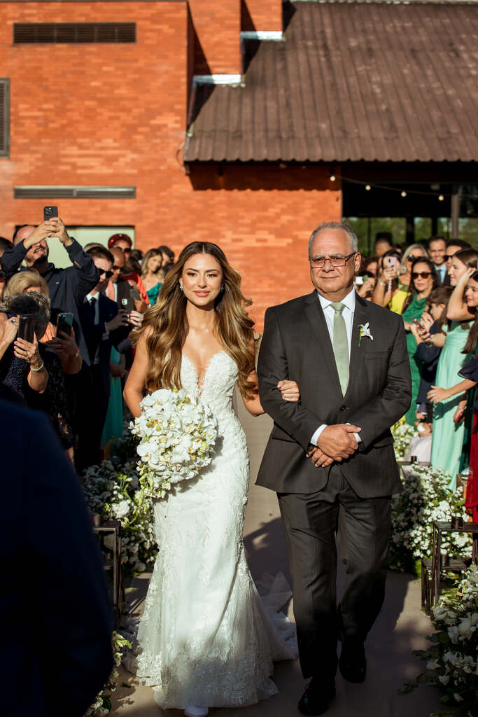 entrada da noiva com vetsido sereia e buquê redondo branco ao lado do pai com terno preto e gravata cinza
