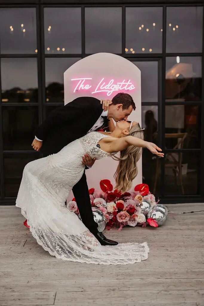noivos se beijando na frente de paineld e fotos com lereiro neon rosa