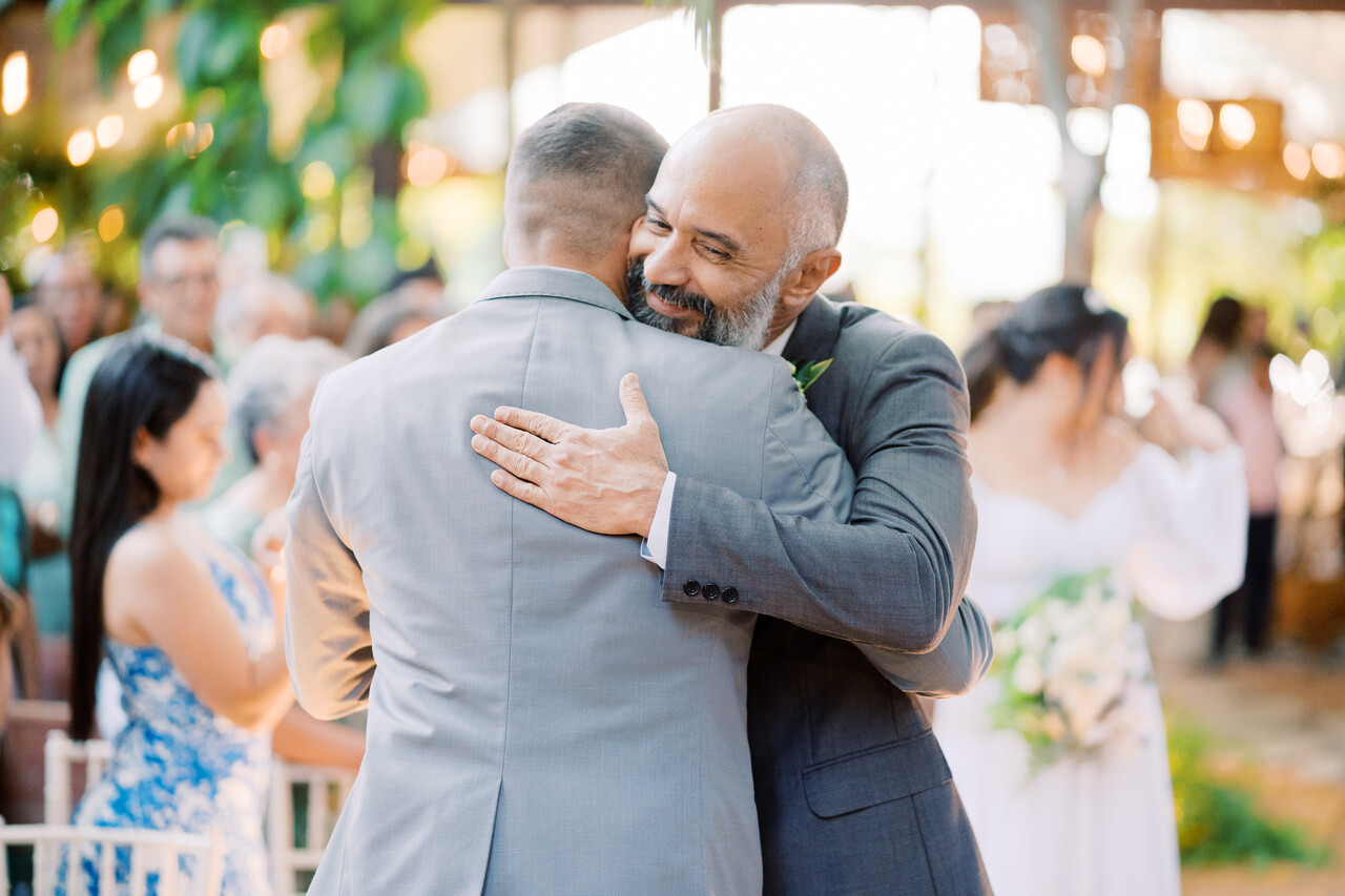 pai da noiva com terno cinza médio abraçando o noivo com terno cinza