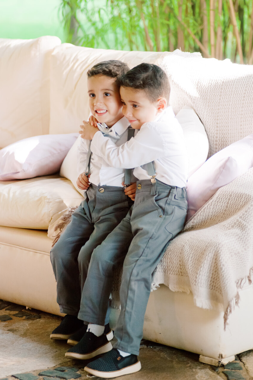 dois pajens com camisa de manga longa branca calça e suspensório cinza se abraçando no sofá