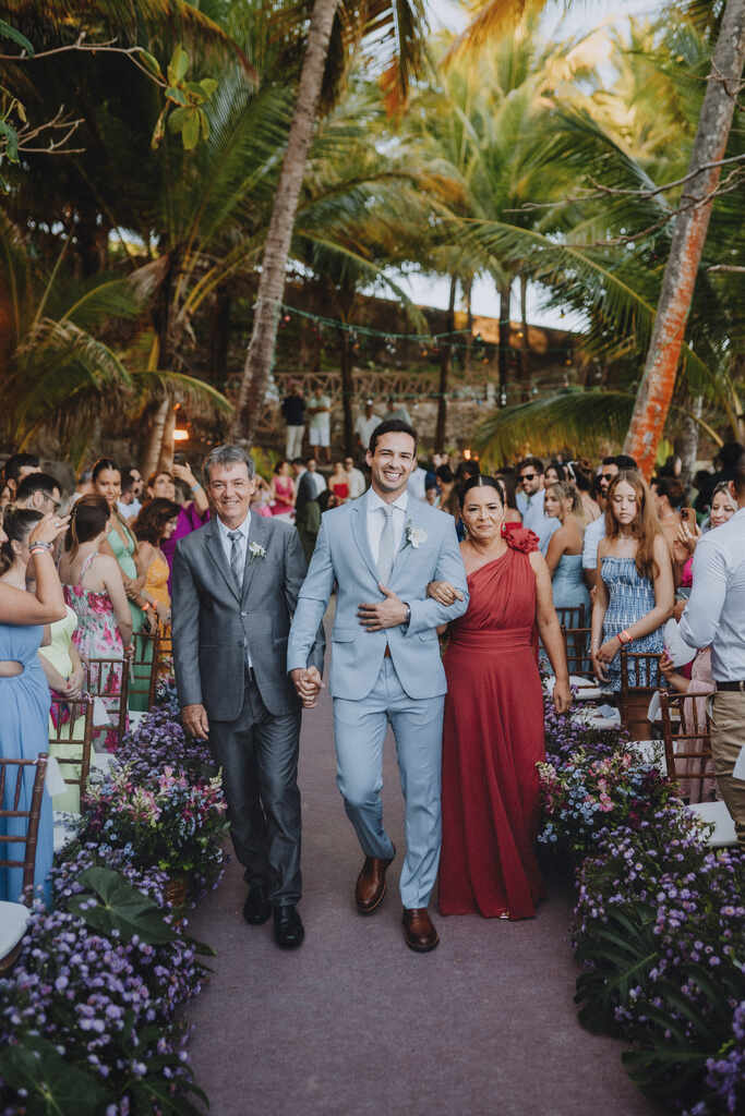 entrada do noivo com tenro azul claro com o pai com tenro cinza chumbo e mãe com vestido vermelho com ombro único