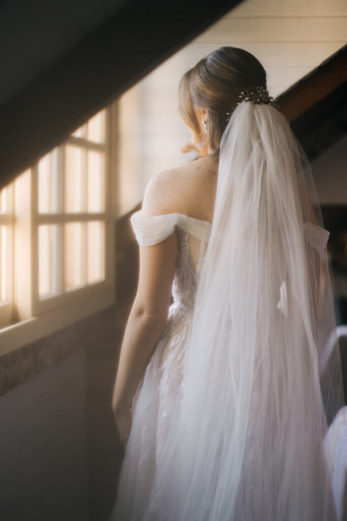 mulher com vestido de noiva com manga e véu volumoso dentro do quarto rústico