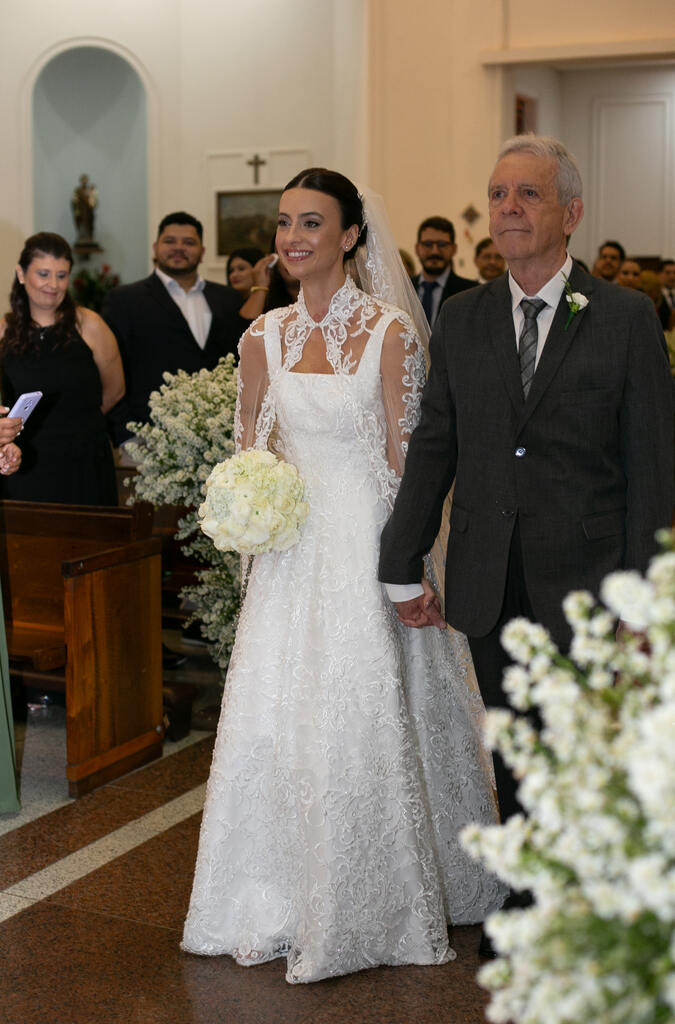 entrada da noiva com buquê redodno com rosas brancas ao lado do pai com terno preto