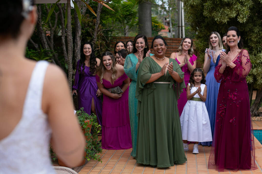 madrinhas com vestido verdes azuis e roxos reagindo à noiva