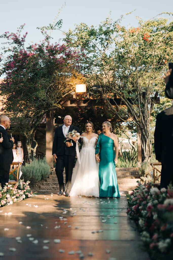 entrada da noiva com buquê ao lado do pai com terno preto e mãe com vetsido verde esmeralda