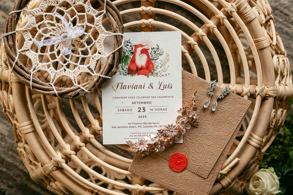 convite de casamento com aquarela de raposas ao lado de porta alianças de macramê e grinalda floral e brincos em cima de mesa rustica