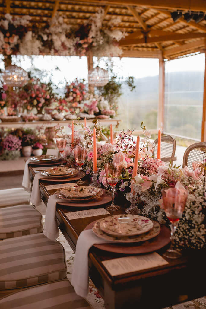 mesa comunitária com mesa posta e velas cor de rosa e flores no centro