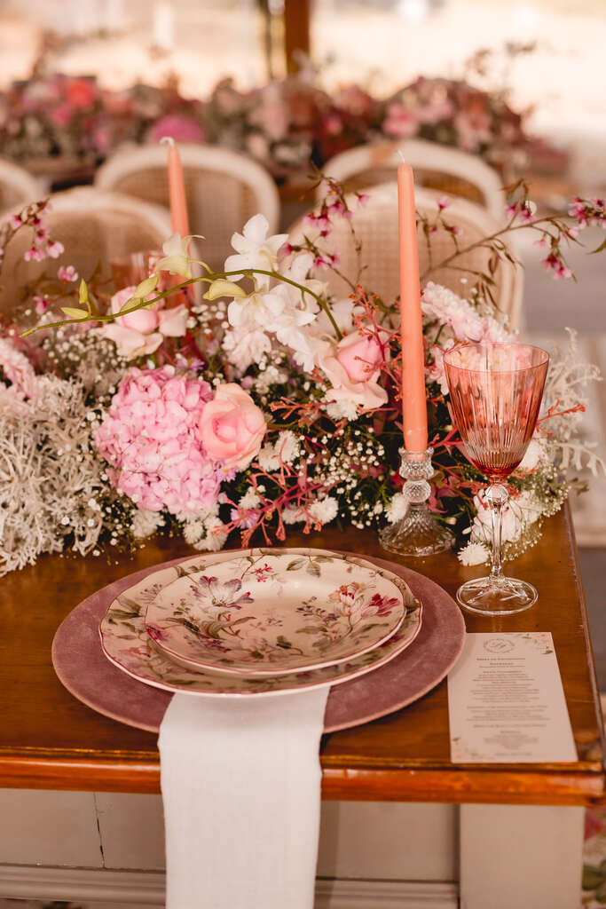 mesa posta com prato com estampa floral e vela cor de rosa e flores no centro