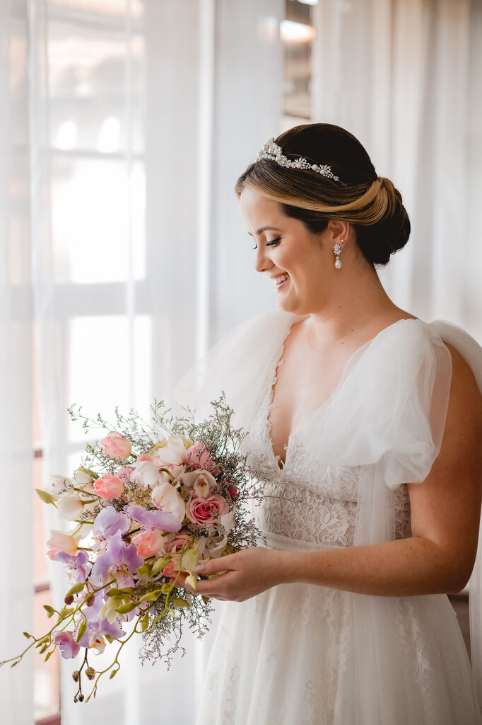 noiva com vestido com decote em v e manga bufante segurando buquÊ com flores brancas liláses e rosas