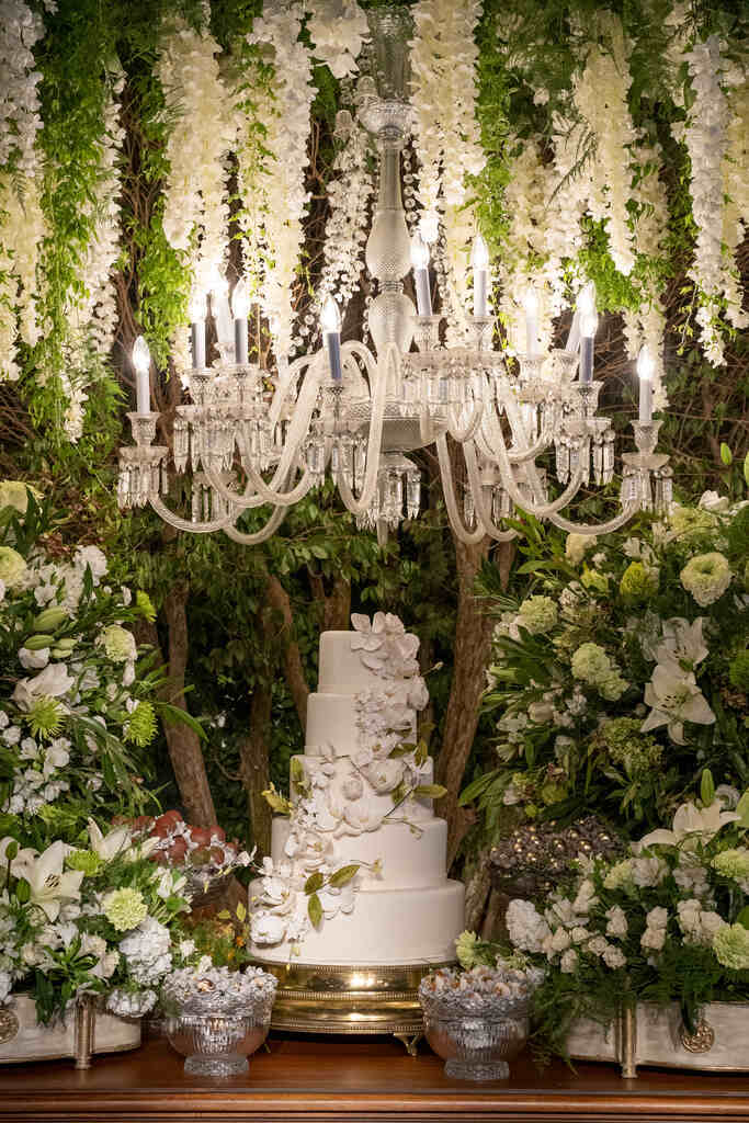 mesa do bolo clássica com bolo de casamento com quatro andares e topo de flores e lustre luxuoso