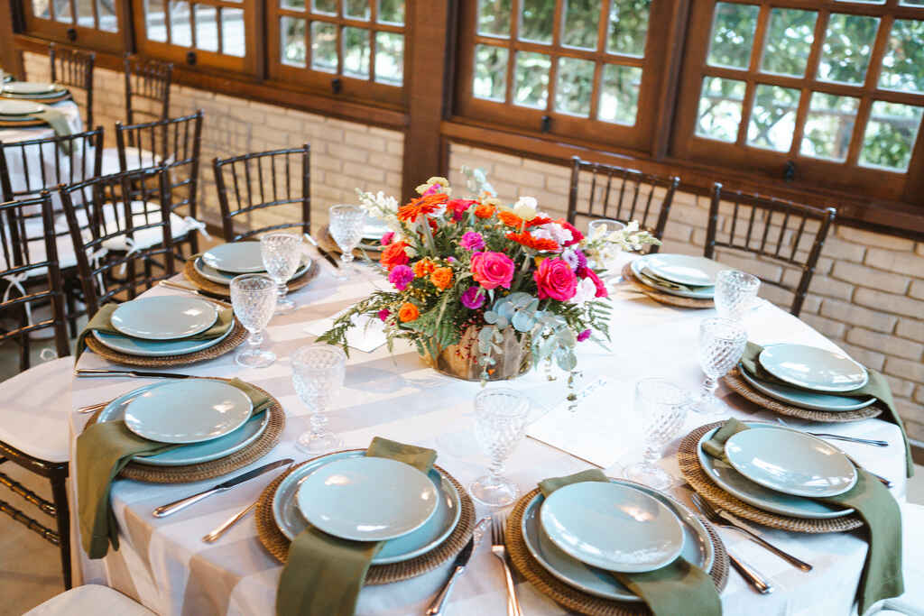 mesa posta com pratos e guardanapos verdes e arranjo no centro com flores laranjas e rosas