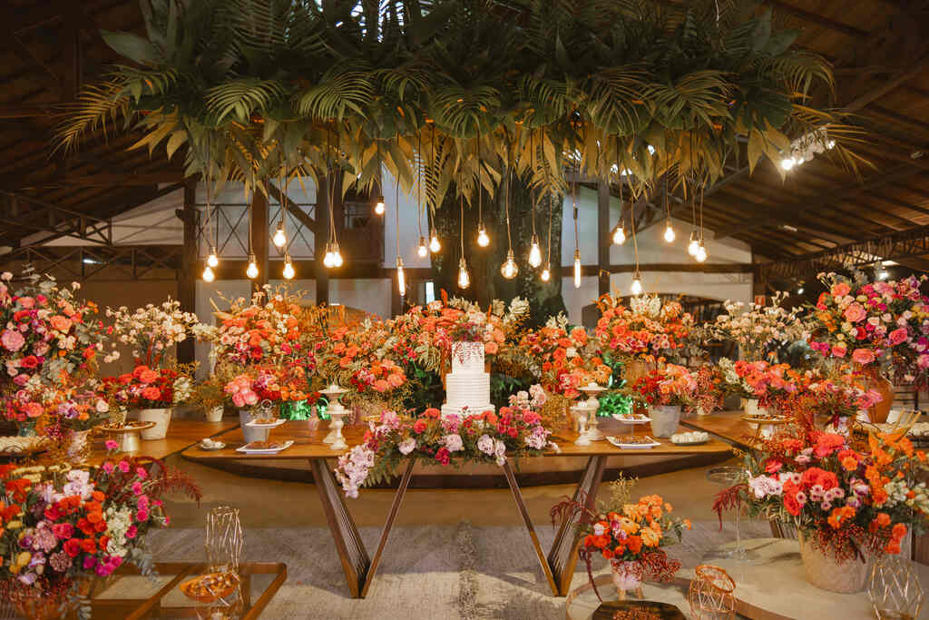 mesa com bolo de casamento branco decorada com flores vermelhas rosas e laranjas