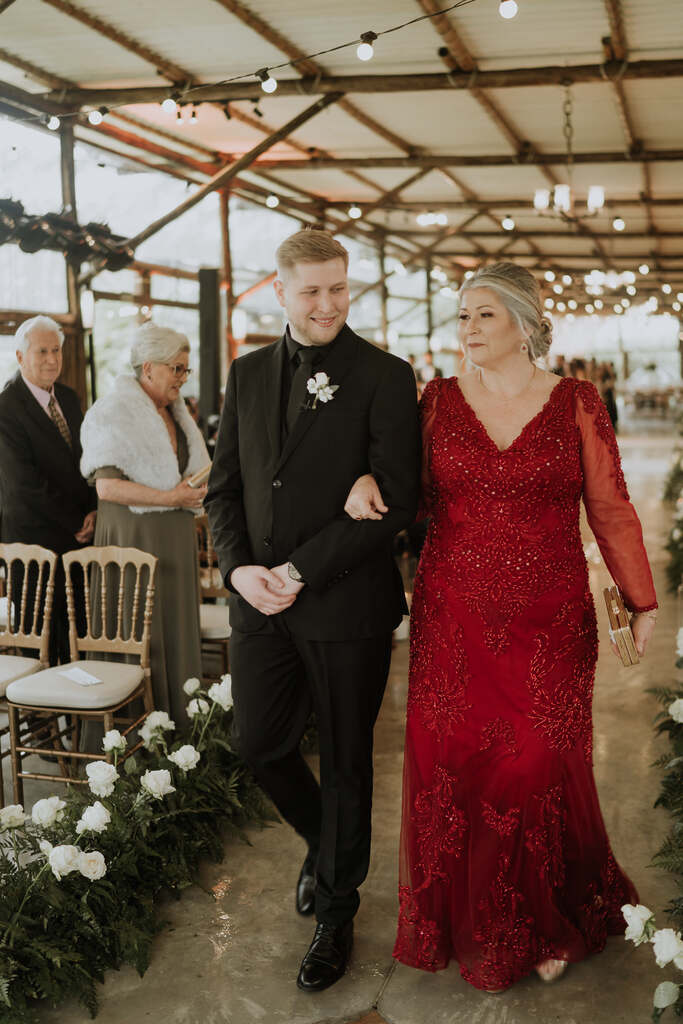 entrada do noivo com terno preto com a mãe com vestido vermelho com mangas