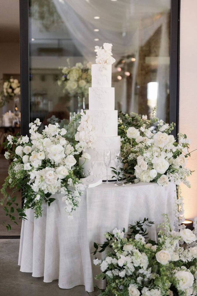 mes redonda branca com bolo de casamento e flores brancas em volta