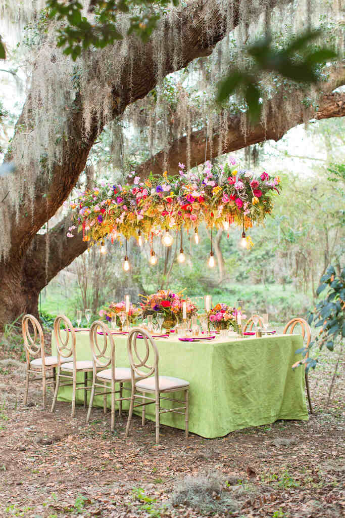 mesa com toalha verde com arranjo pendente com flores vermelhas laranjas e roxas no campo
