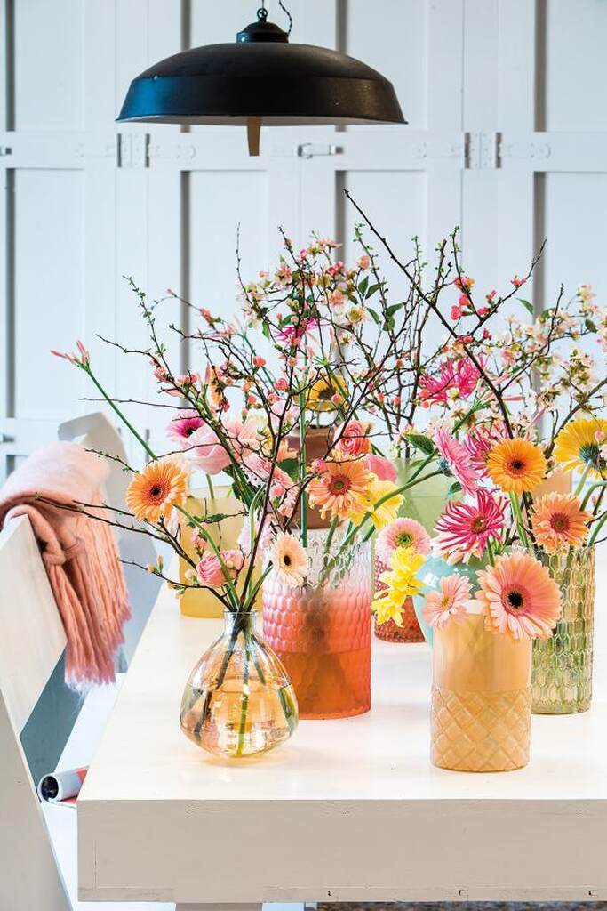 mesa branca com vasos com gérberas rosas amarelas e laranjas