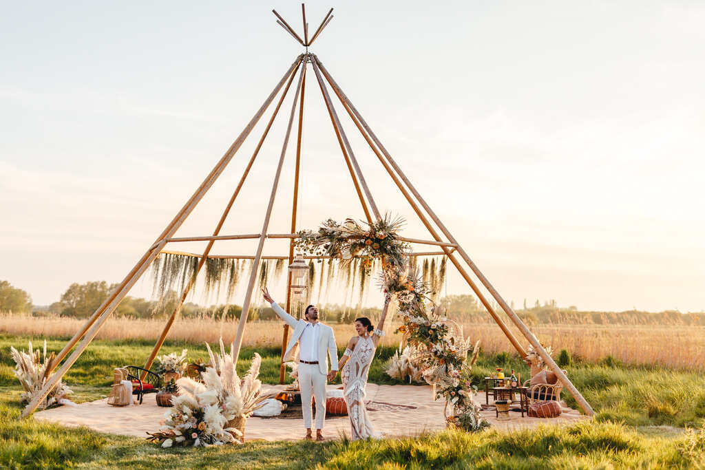casal comemorando sob estrutura tipo cabana de maidera com decoração boho no campo