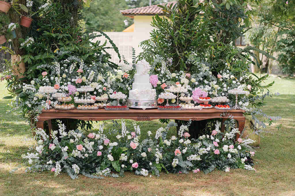 mesa com bolo de casamento romântica com bandejas de doces e flores brancas amarelas e rosas