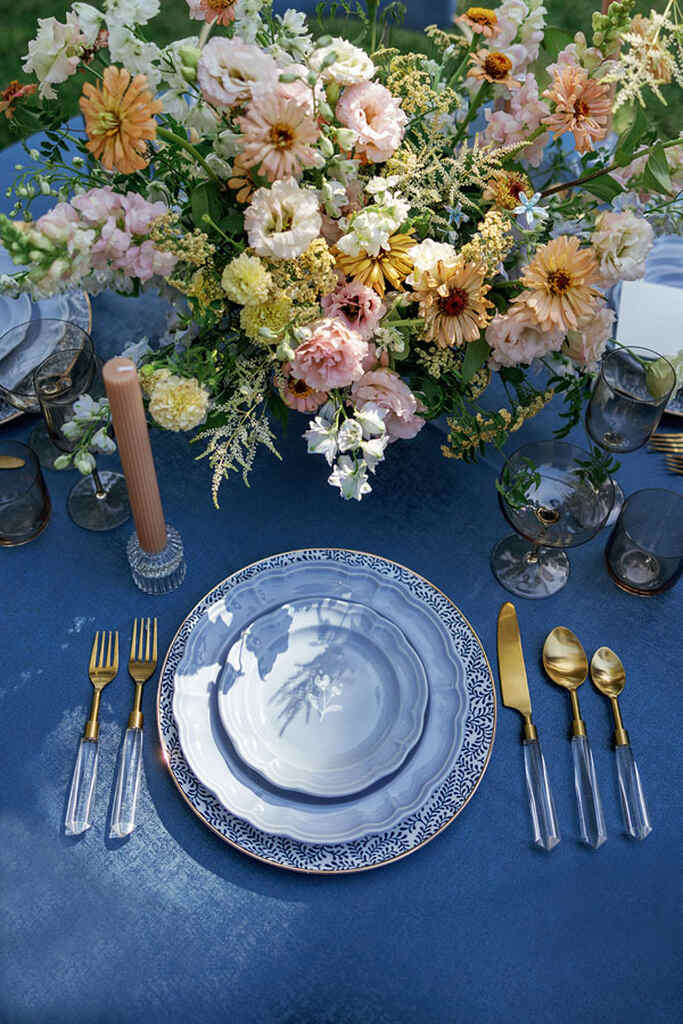 mesa posta azul com vela rosê e flores coloridas no centro
