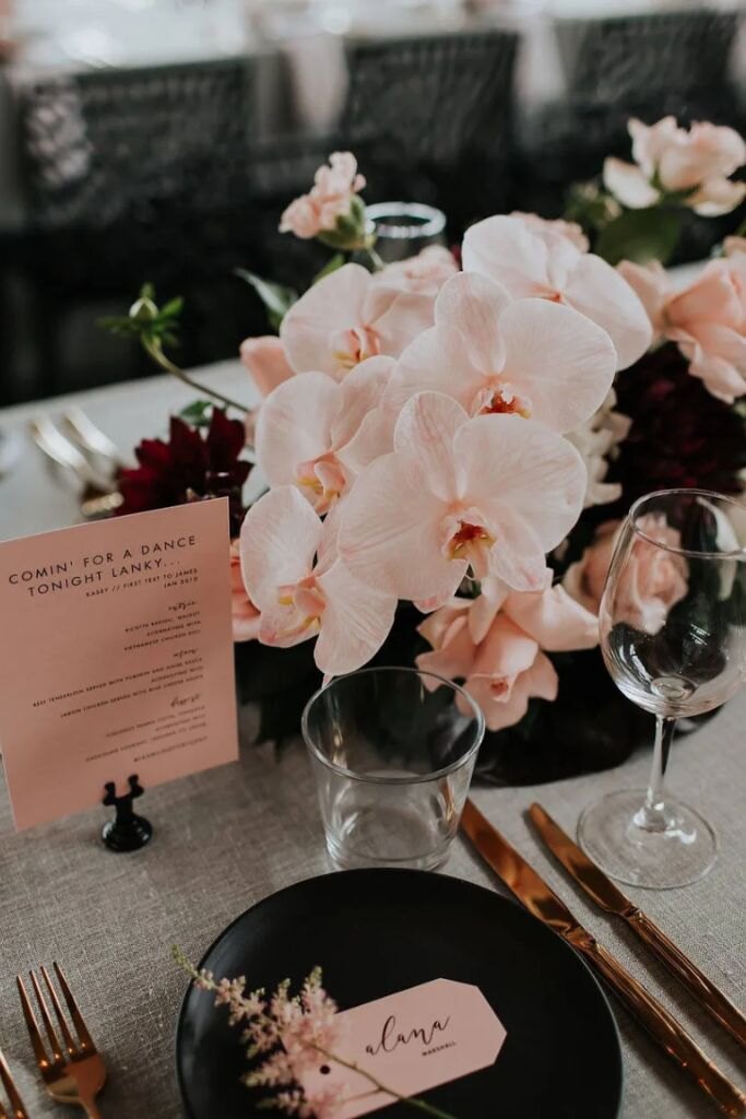 mesa posta com prato preto com orquideas rosa