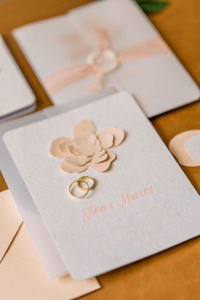 convite de casamento com flor de papel na cor peach fuzz com alianças em cima