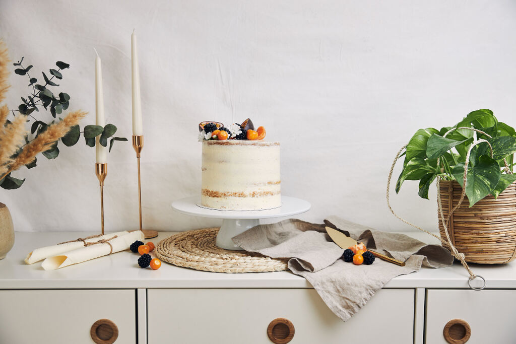 mesa minimalista com bolo de casamento simples e ao lado velas e vaso com plantas