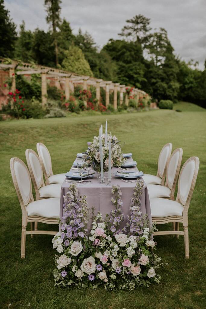 mesa com toalha lilás com decor delicada e romântica e flores na base da mesa