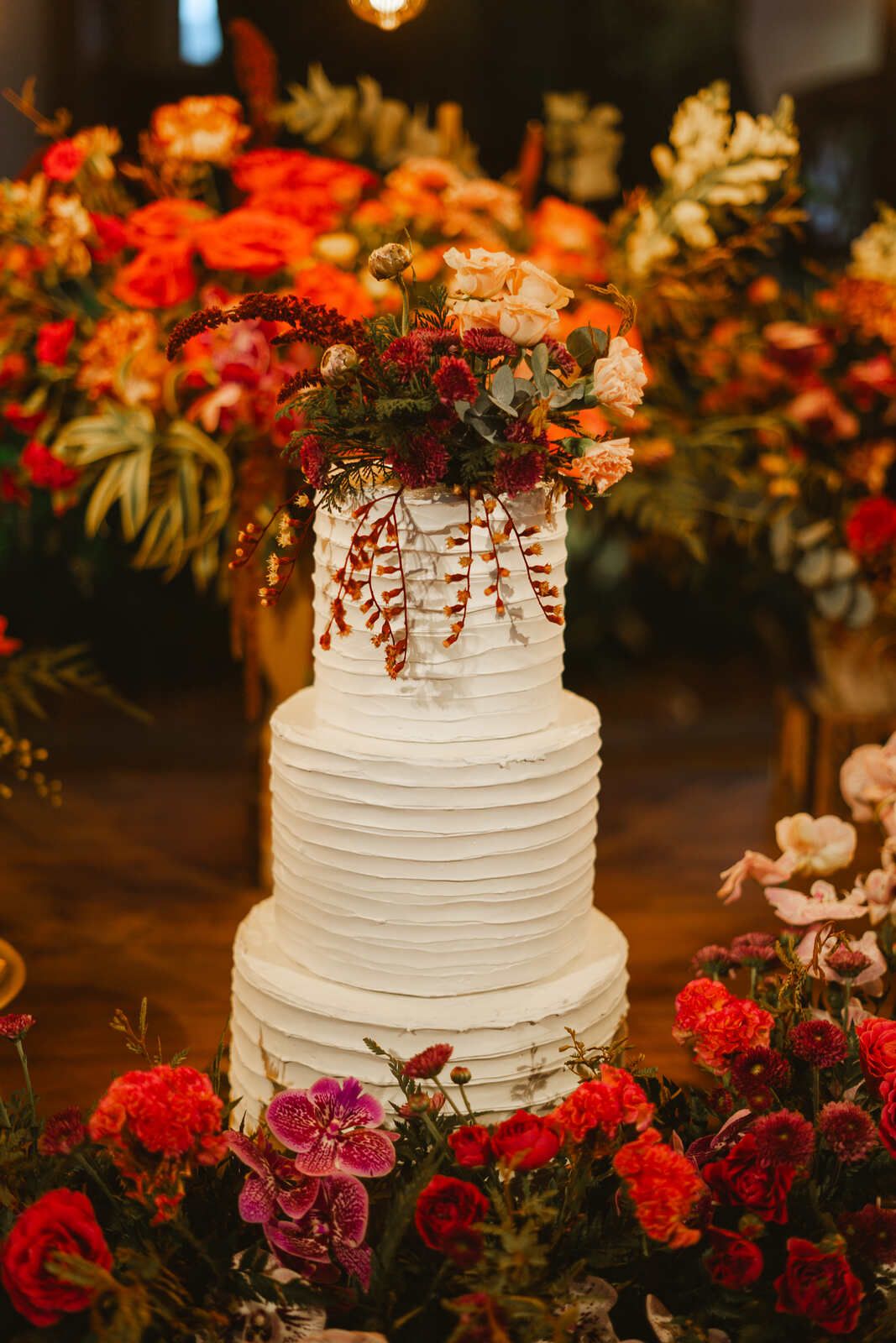 bolo de casamento branco com três andares com flores laranjas e vermelhas no topo