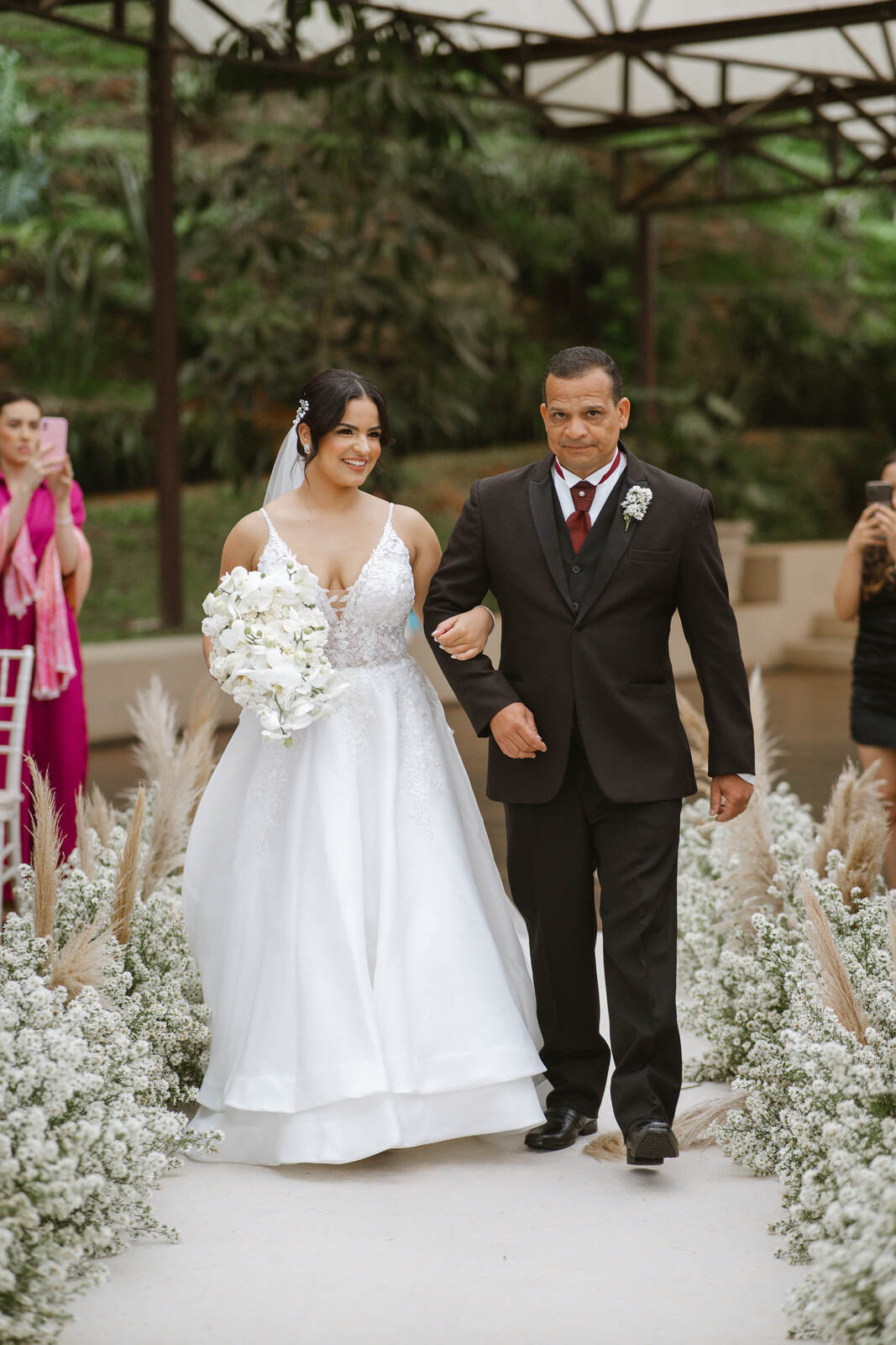 entrada da noiva com buquÊ de orquideas brancsa ao lado do pai com terno preto com gravata vermelha