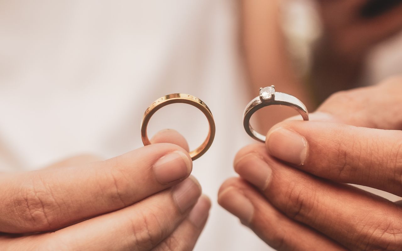 mãos segurando aliança de casamento dourada e anel de noivado solitário em ouro branco