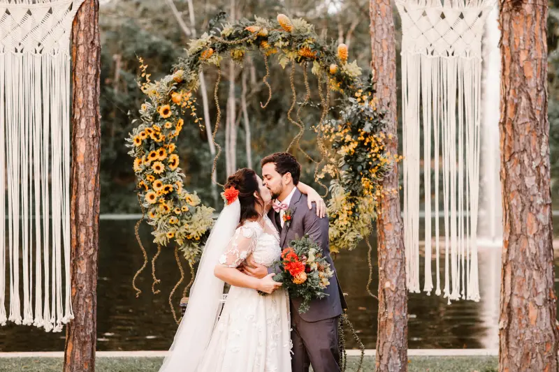 altar de casamento girassol e macram&ecirc; com noivos em frente se beijando