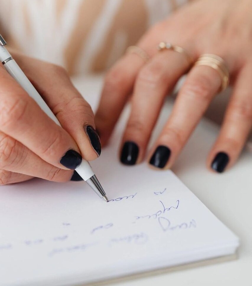 mão feminina escrevendo mensagem de casamento com caneta azul em papel branco