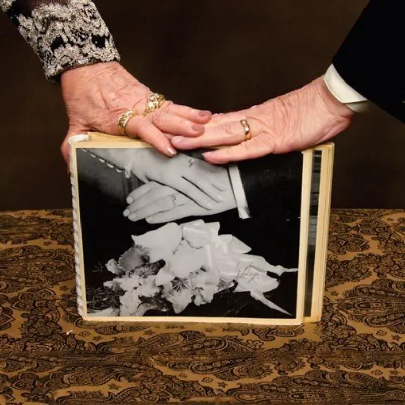 casal com as mãos em cima da foto de casamento mostrando as alianças de casamento