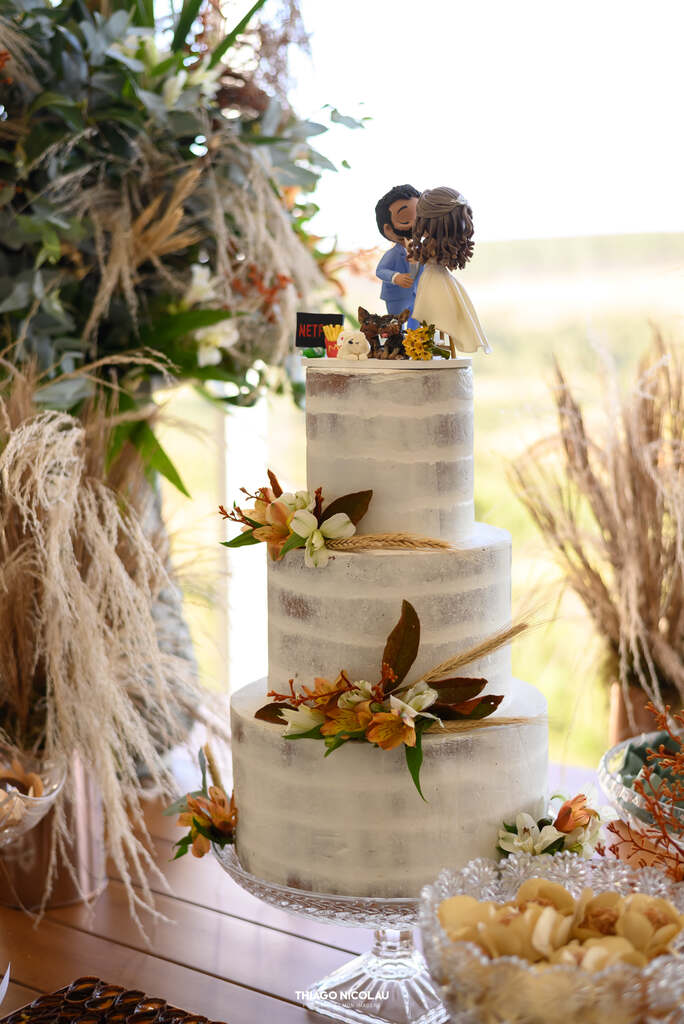 mesa com bolo de casamento branco semiespatulado com flores e topo de bolo com bonecos e cachorros