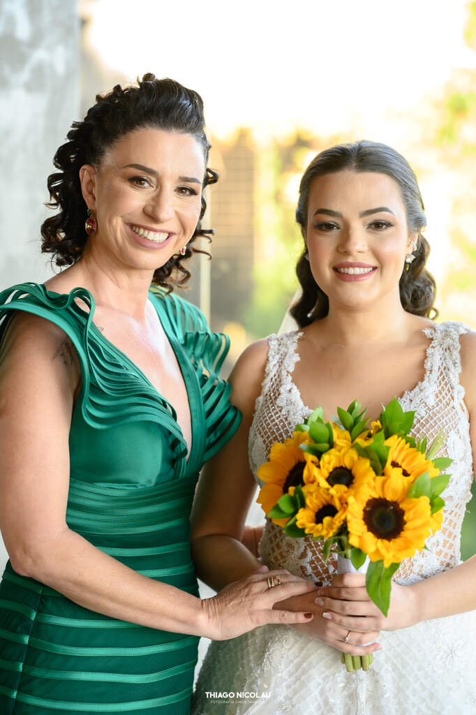 mãe da noiva com vestido verde esmeralda ao lado da novia com buquê de girassol