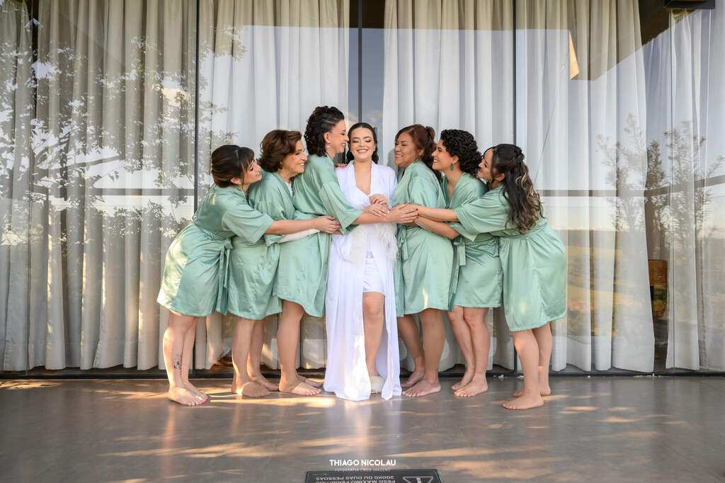 seis madrinhas com robes na cor verde sage abraçando a noiva com robe longo branco