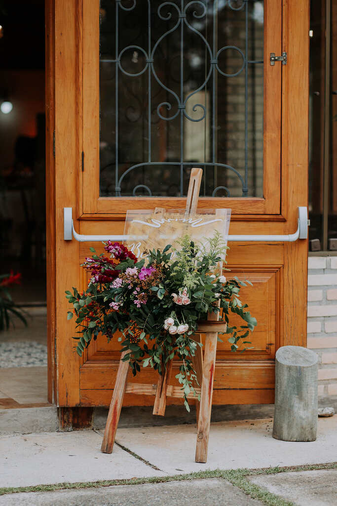 cavalete de madeira com plantas e flores rosas na frente da porta