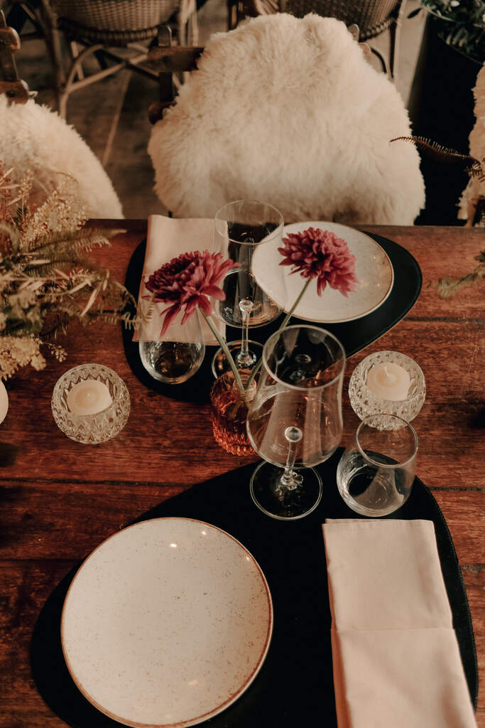 mesa posta com jogo americano preto e vasos de vidro com flores cor de rosa