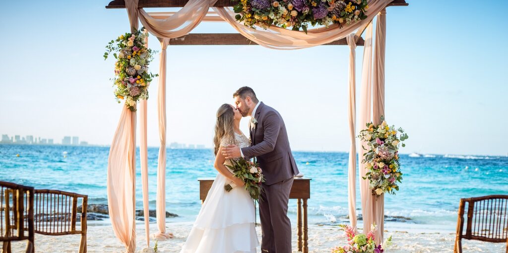 casal de noivos se beijando sob altar em casamento pé na areia em cancún