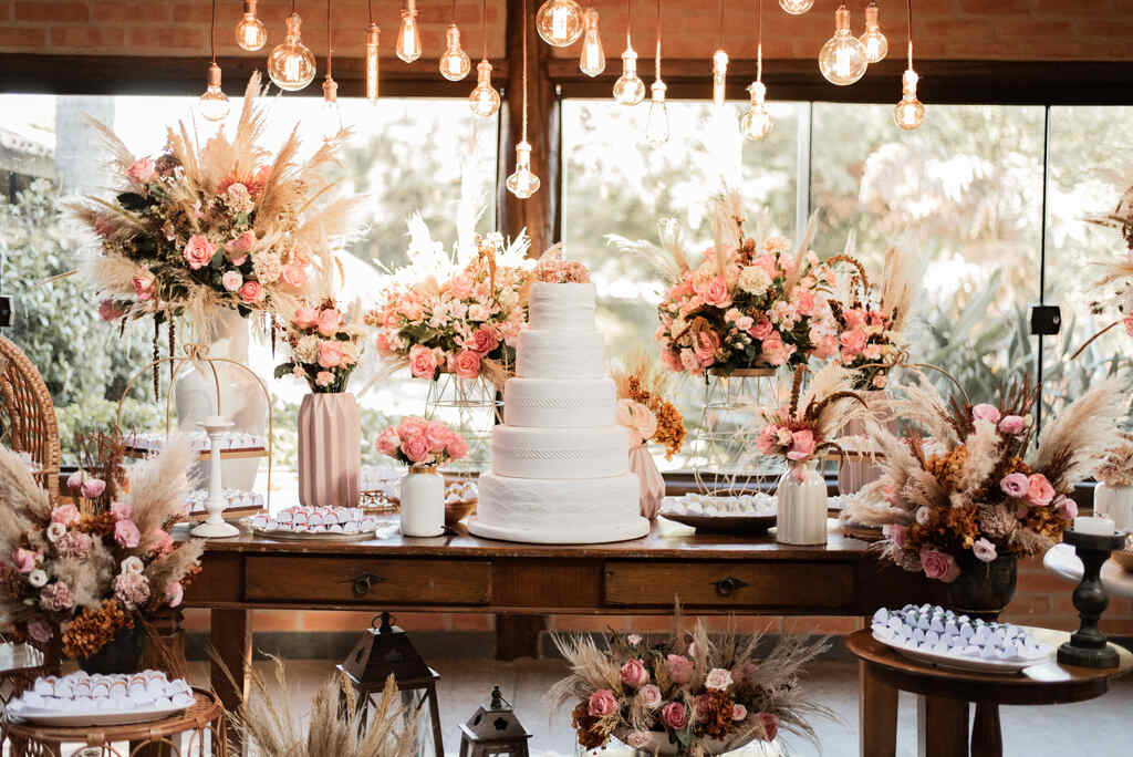 mesa do bolo decorada com rosas cor de rosa e capim dos pampas no salão