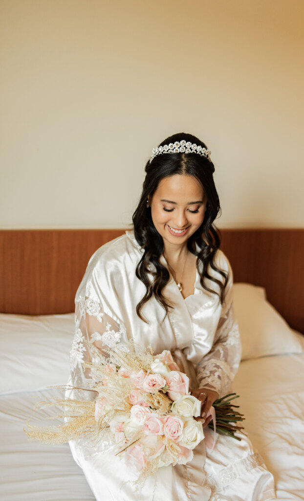 noiva com robe branco acetinado com tiara sentada na cama